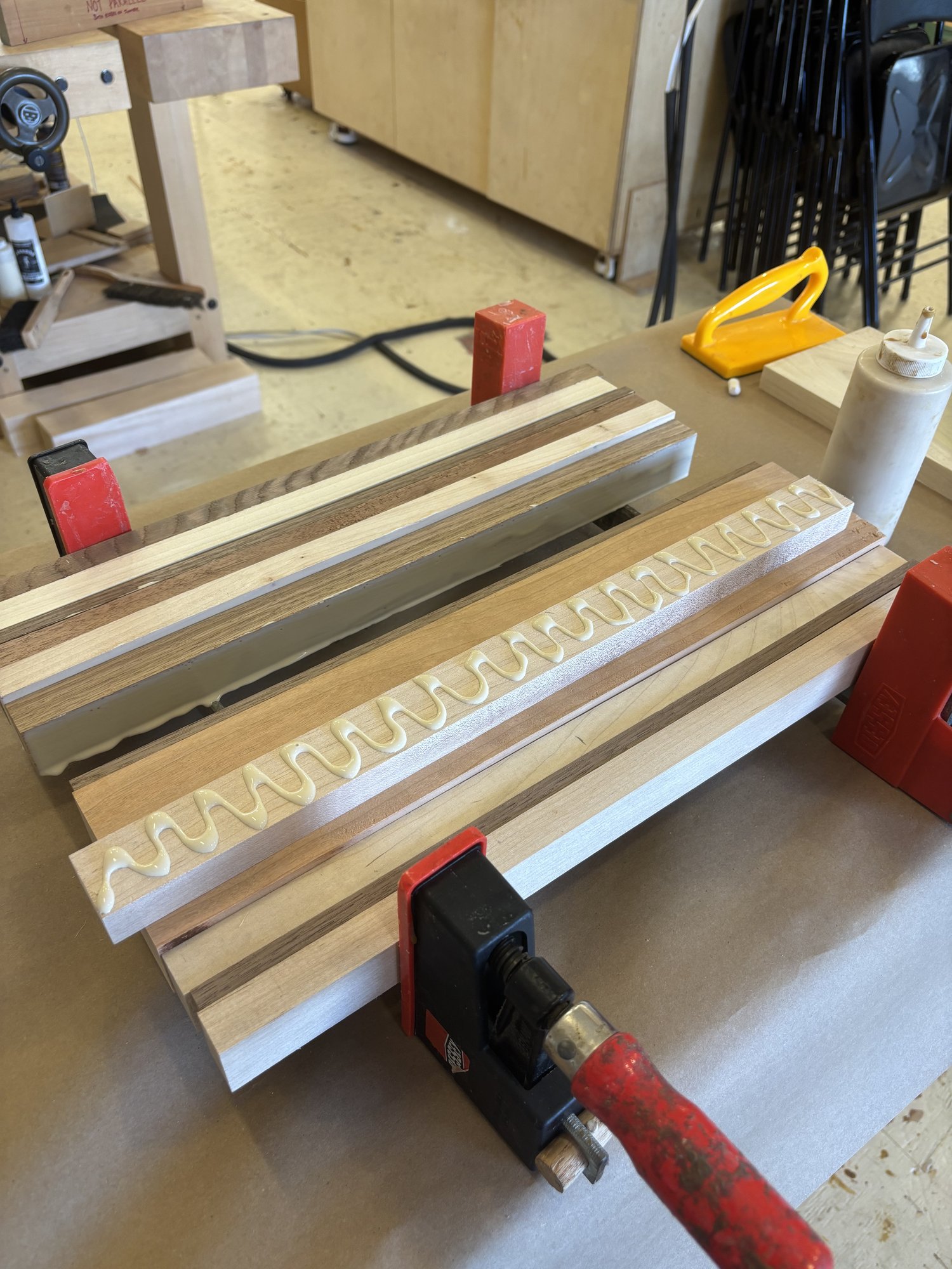 Glue beads laid down on the strips just before assembly. Each piece gets a continuous zigzag bead, calibrated to give full coverage without flooding the seam.