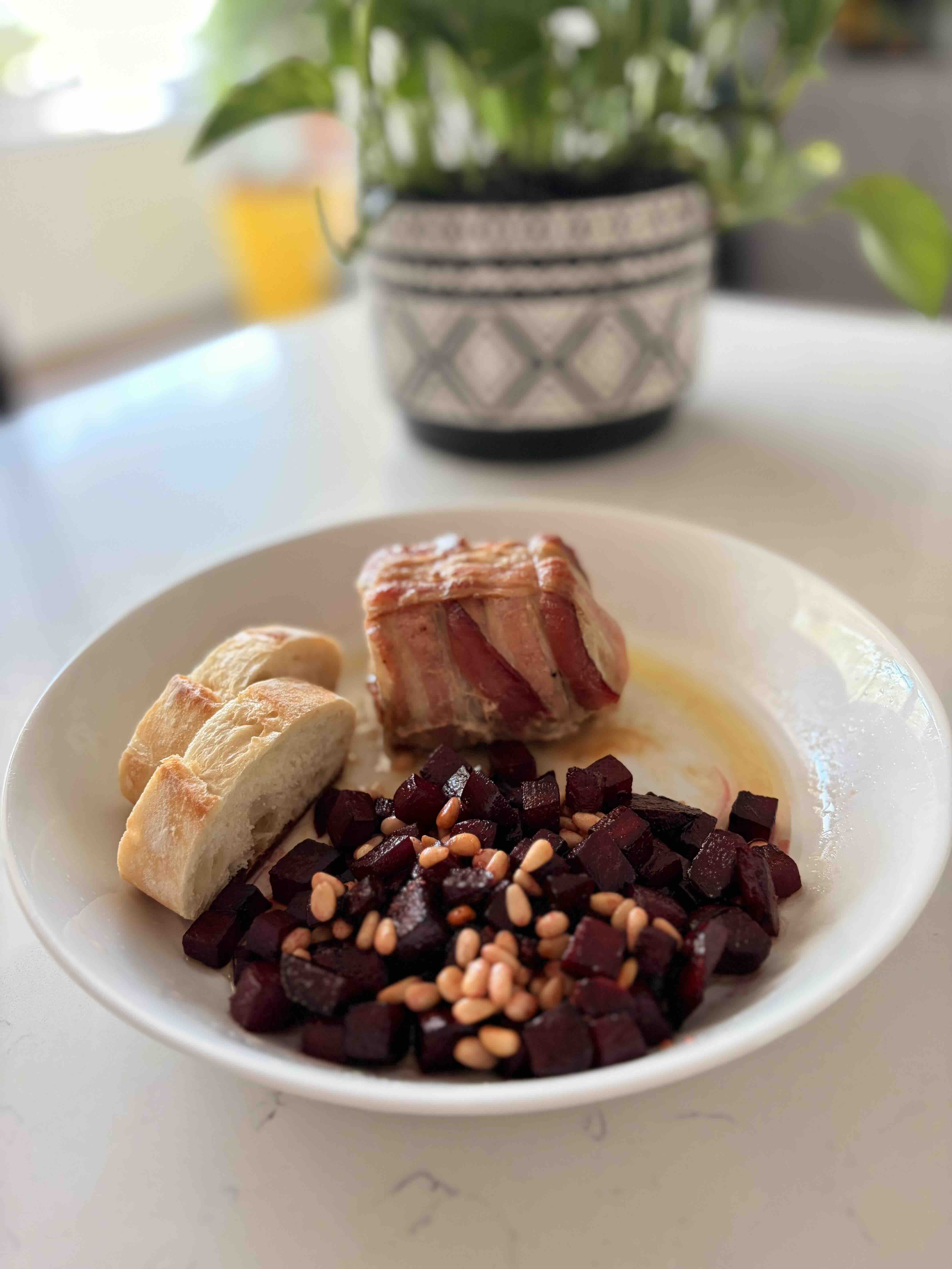 Sliced bacon-wrapped pork loin on a plate beside a small mound of cubed beets glazed in butter and pine nuts.
